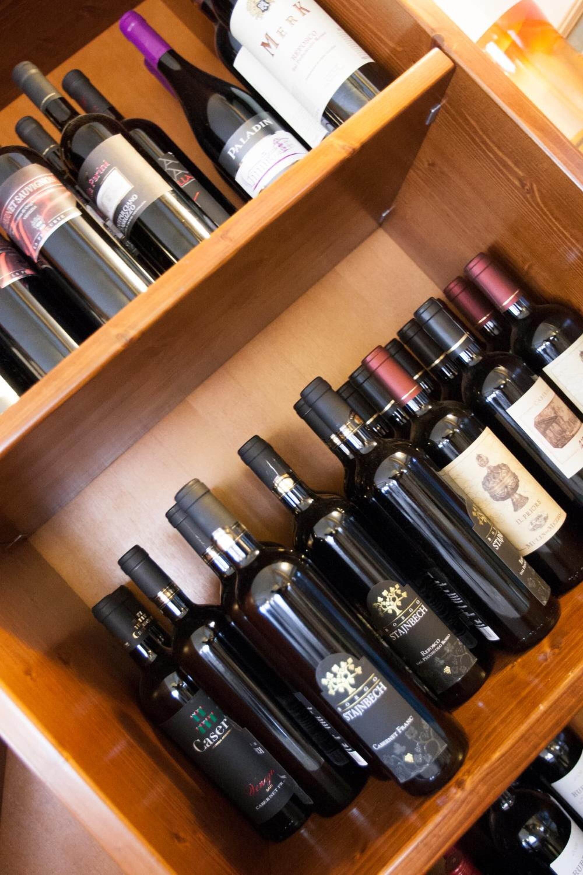 Un porte-bouteilles en bois contenant plusieurs bouteilles de vin, dont des marques comme Casillero del Diablo et Stainbeck.