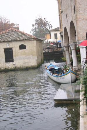 A narrow canal with a boat docked at a stone building. - Hotel Alla Botte (Portogruaro)