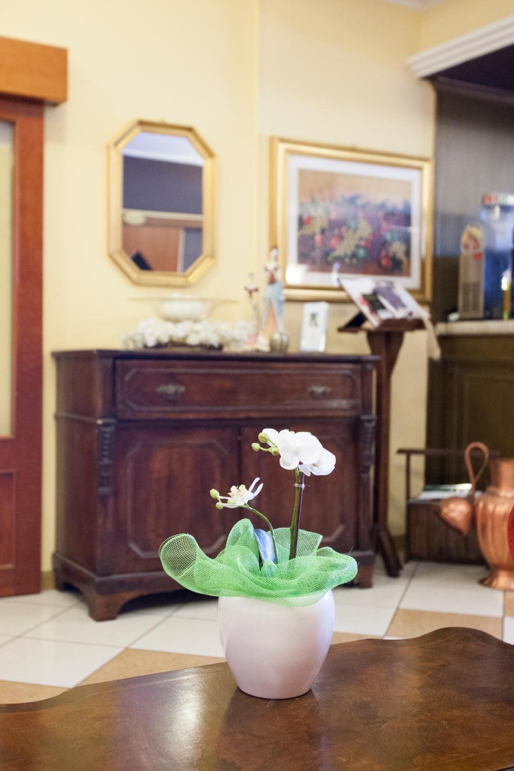 Una habitació amb una taula de fusta, un vas de flors blanc, un mirall i un quadre a la paret.