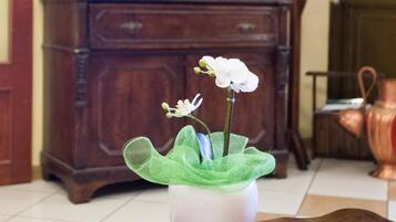 Una habitació amb una taula de fusta, un vas de flors blanc, un mirall i un quadre a la paret.