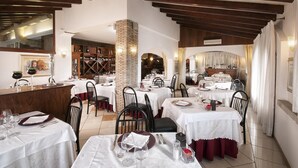 Ein Restaurant mit mehreren gedeckten Tischen, einem Weinkühlschrank im Hintergrund und einer Ziegelstütze.