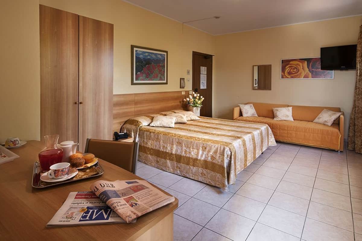 Habitación de hotel con cama, sofá, mesa de comedor con desayuno y televisor en la pared.