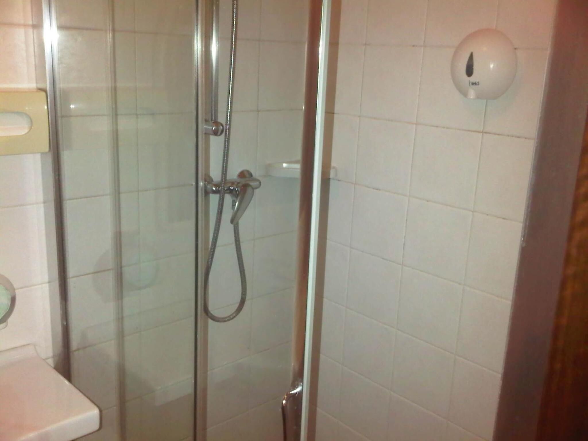 Ducha con cerramiento de vidrio, cabezal de ducha de mano y dispensador de jabón empotrado.