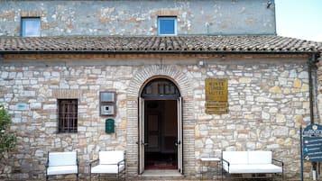 A stone building with a sign for Monte Conero Hotel, a restaurant, and an American Bar. There are two white chairs outside.