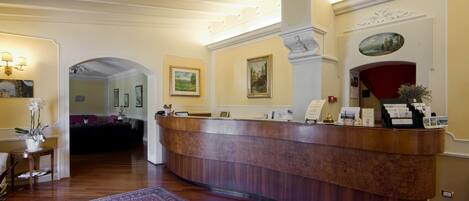 A reception area with a wooden reception desk, a red carpet, and a painting on the wall.