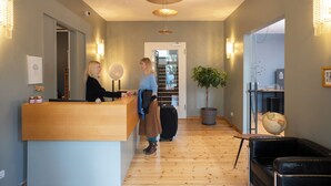 A hotel reception area with a wooden reception desk, a potted plant, a globe, and a black leather sofa. - Hotel Johann (Berlin)