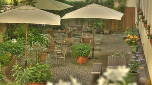 An outdoor patio area with multiple tables and chairs, surrounded by potted plants and umbrellas. - Hotel Johann (Berlin)