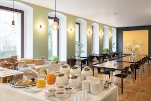 A breakfast buffet with various food items and beverages, a long dining table with chairs, and a large window with natural light. - Hotel Johann (Berlin)