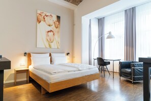A modern hotel room with a wooden bed, a desk, a chair, and a large window with curtains. - Hotel Johann (Berlin)