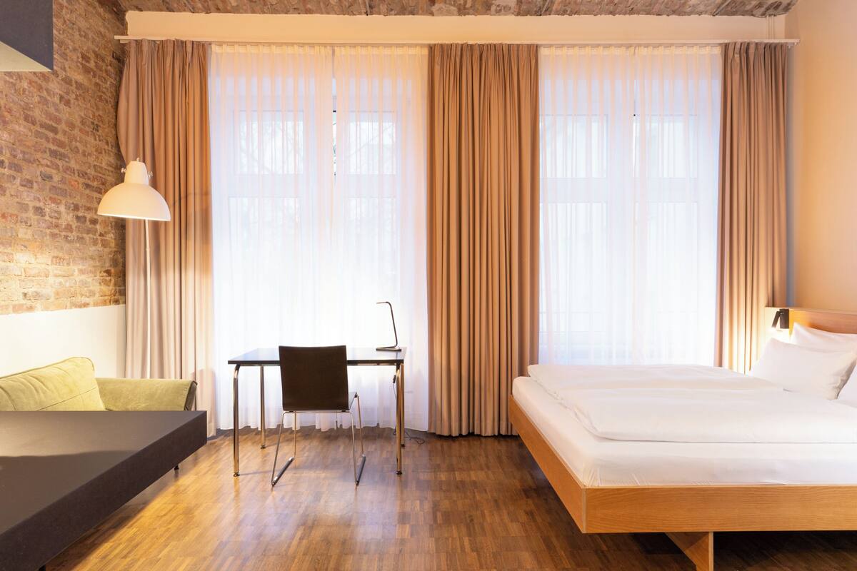 A hotel room with a bed, a desk, a chair, and a lamp.