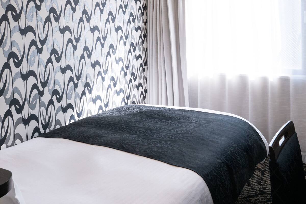 A hotel room with a bed, a desk, and a large window with curtains.