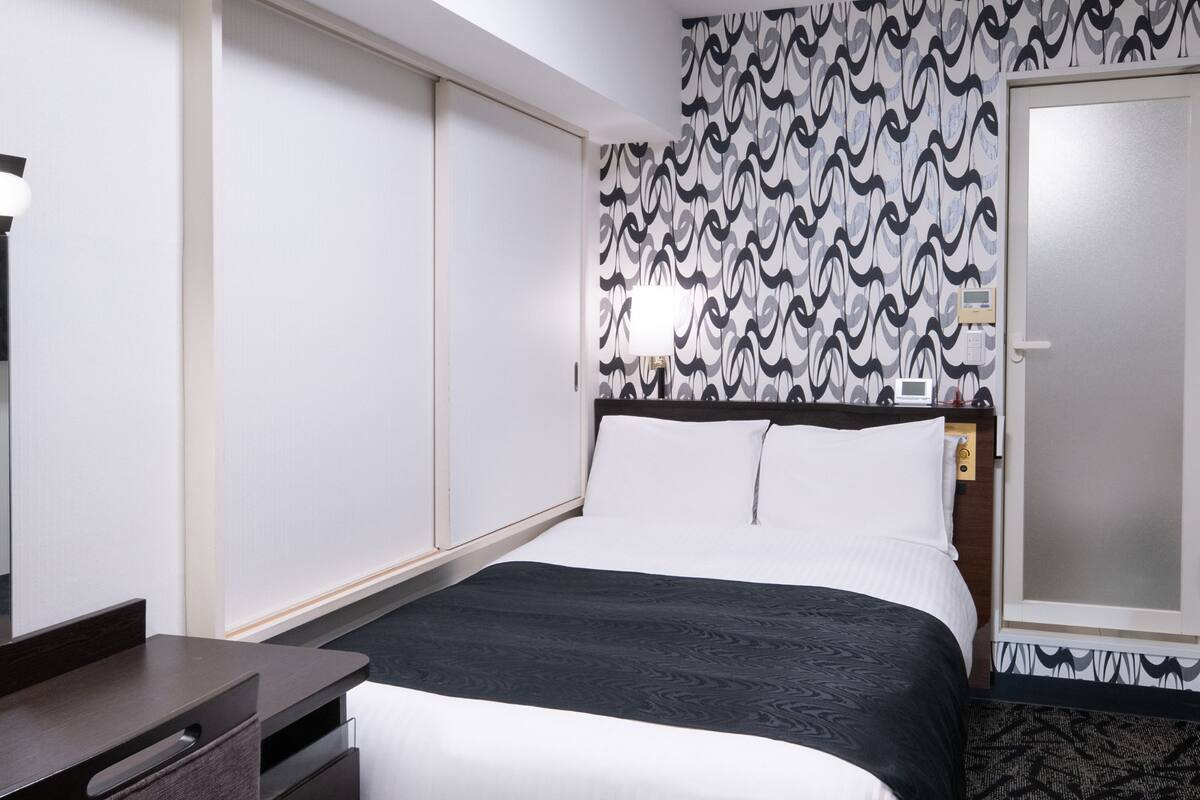 A hotel room with a bed, bedside table, and a wall with a patterned wallpaper.