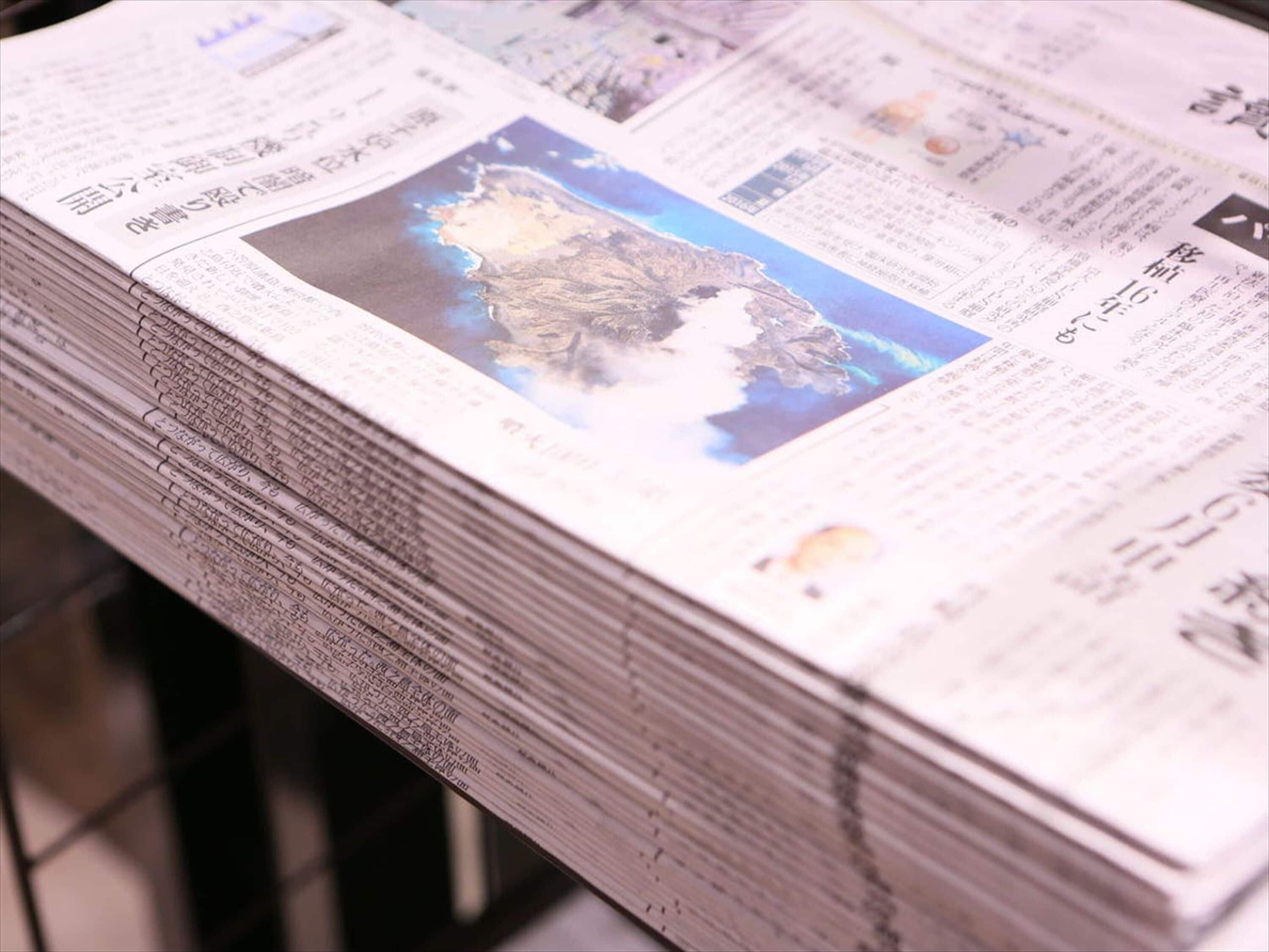 A stack of newspapers with a prominent image of a mountainous landscape.