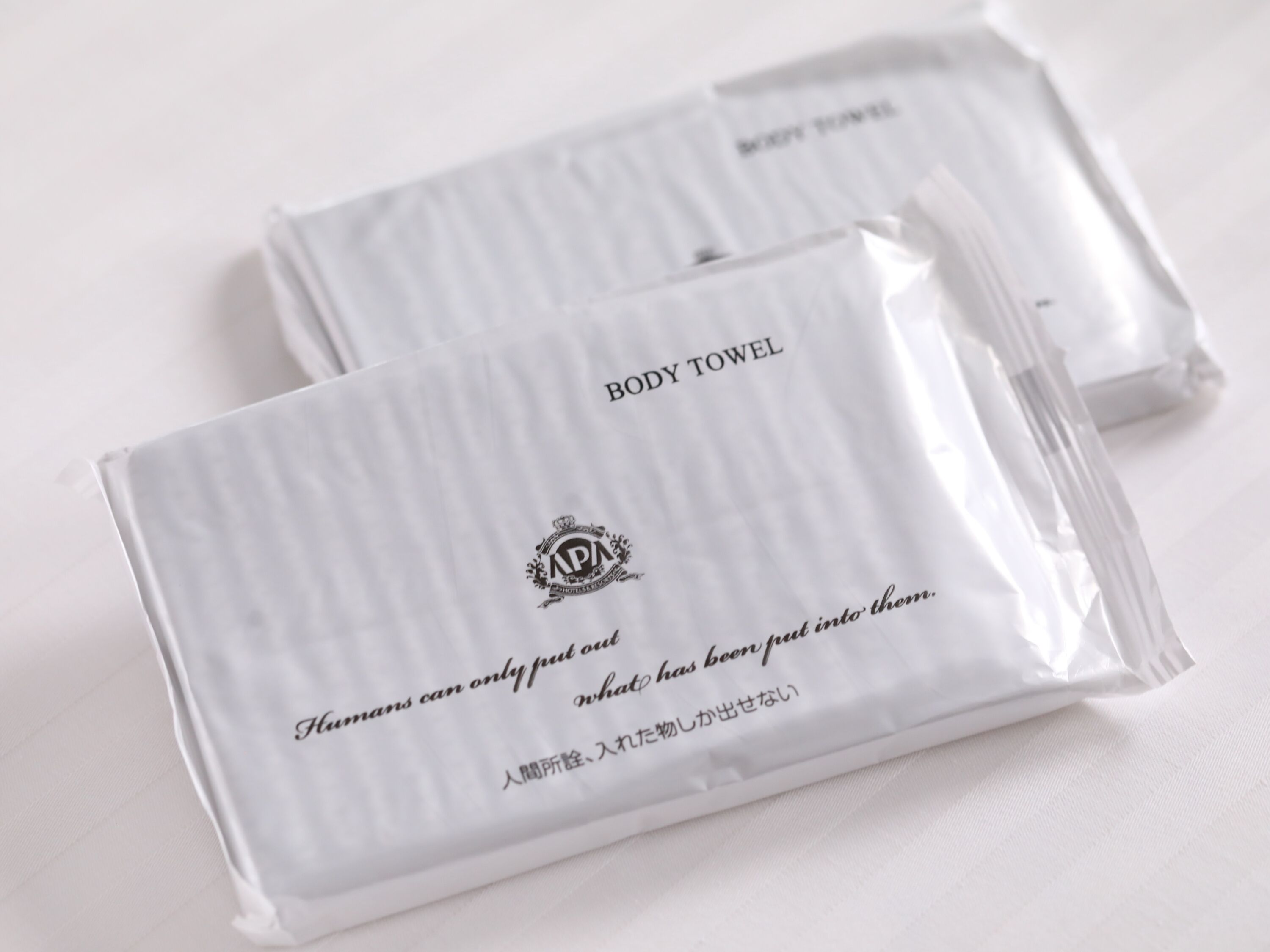 Two white body towels with text and a logo.