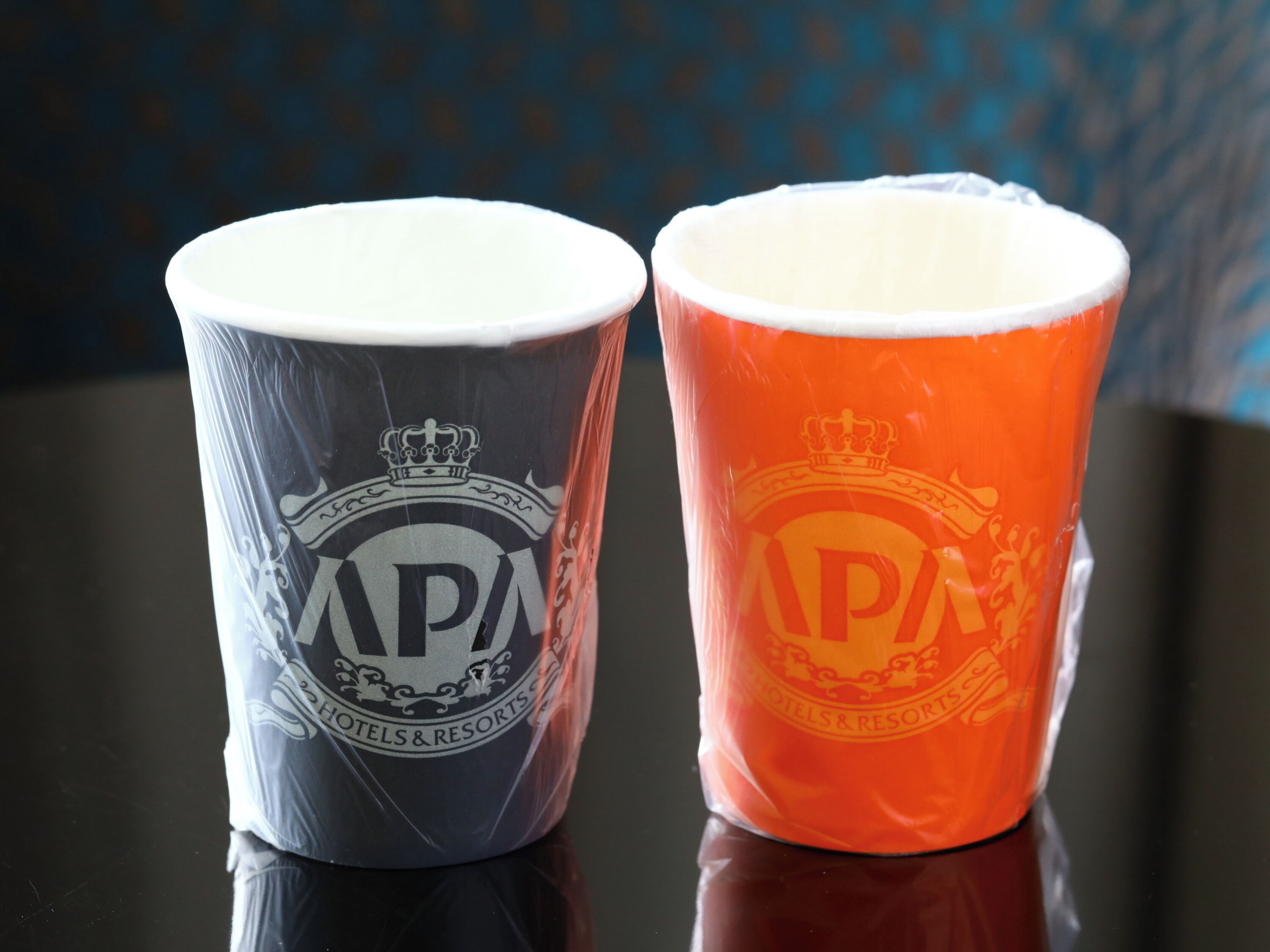 Two cups with embossed logos and text, one with a dark background and the other with an orange background.