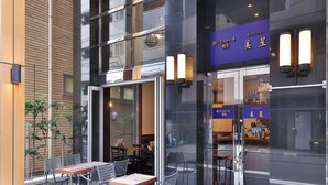 An outdoor seating area with tables and chairs, a glass door entrance, and a sign with Japanese text. - APA Hotel Ningyocho Ekikita (Tokyo)