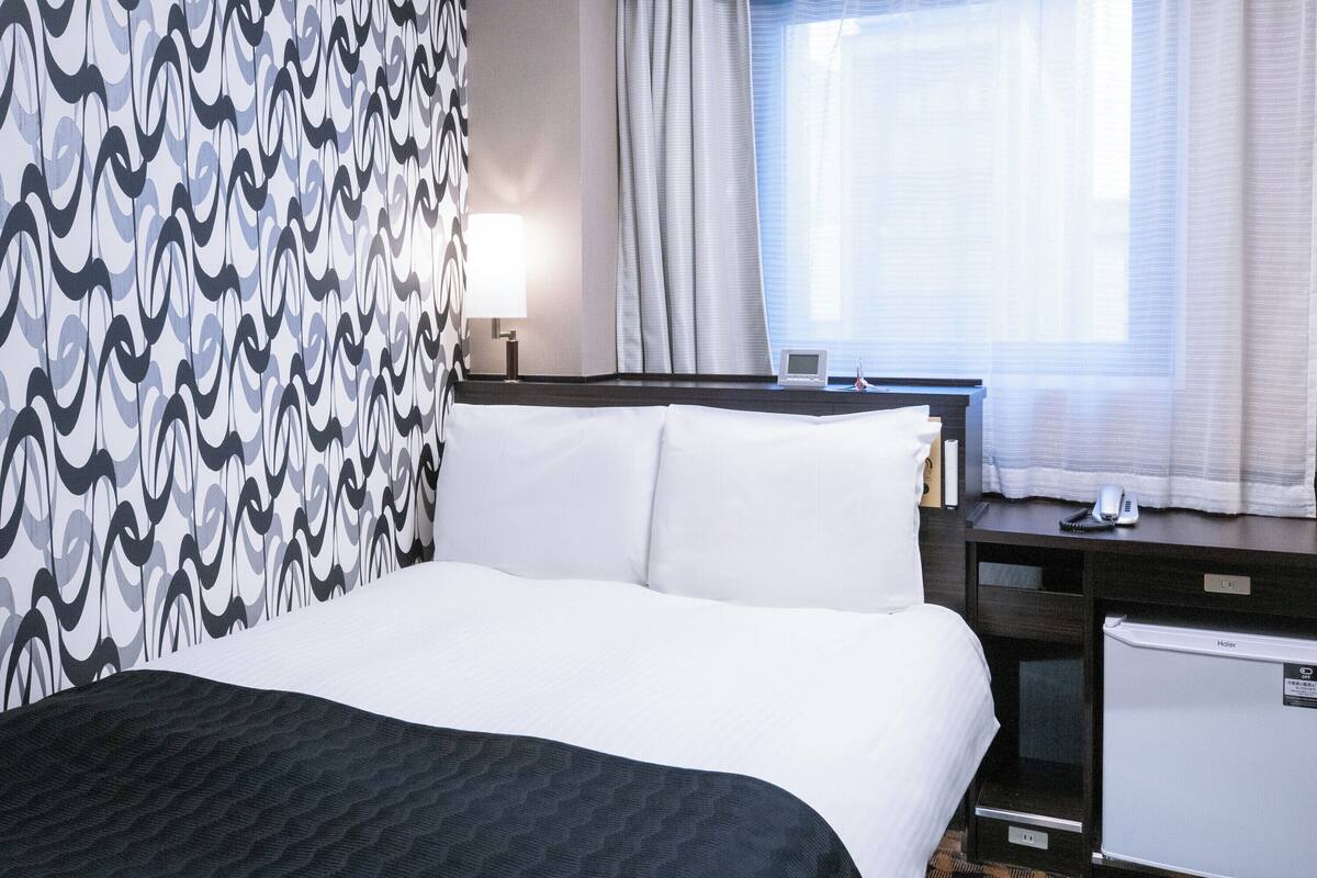 Une chambre d’hôtel équipée d’un lit, d’un bureau, d’une lampe, d’un téléphone et d’un petit réfrigérateur.