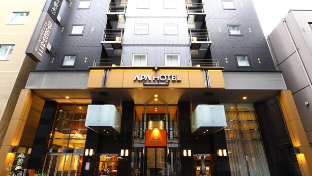 The APA HOTEL entrance with a modern design, featuring a glass facade, a prominent entrance with a sign, and a staircase leading to the upper floors. - APA Hotel Ningyocho Ekikita (Tokyo)