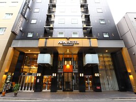 La entrada del APA HOTEL con un diseño moderno, que presenta fachada de vidrio, una entrada destacada con un letrero y una escalera que conduce a los pisos superiores.