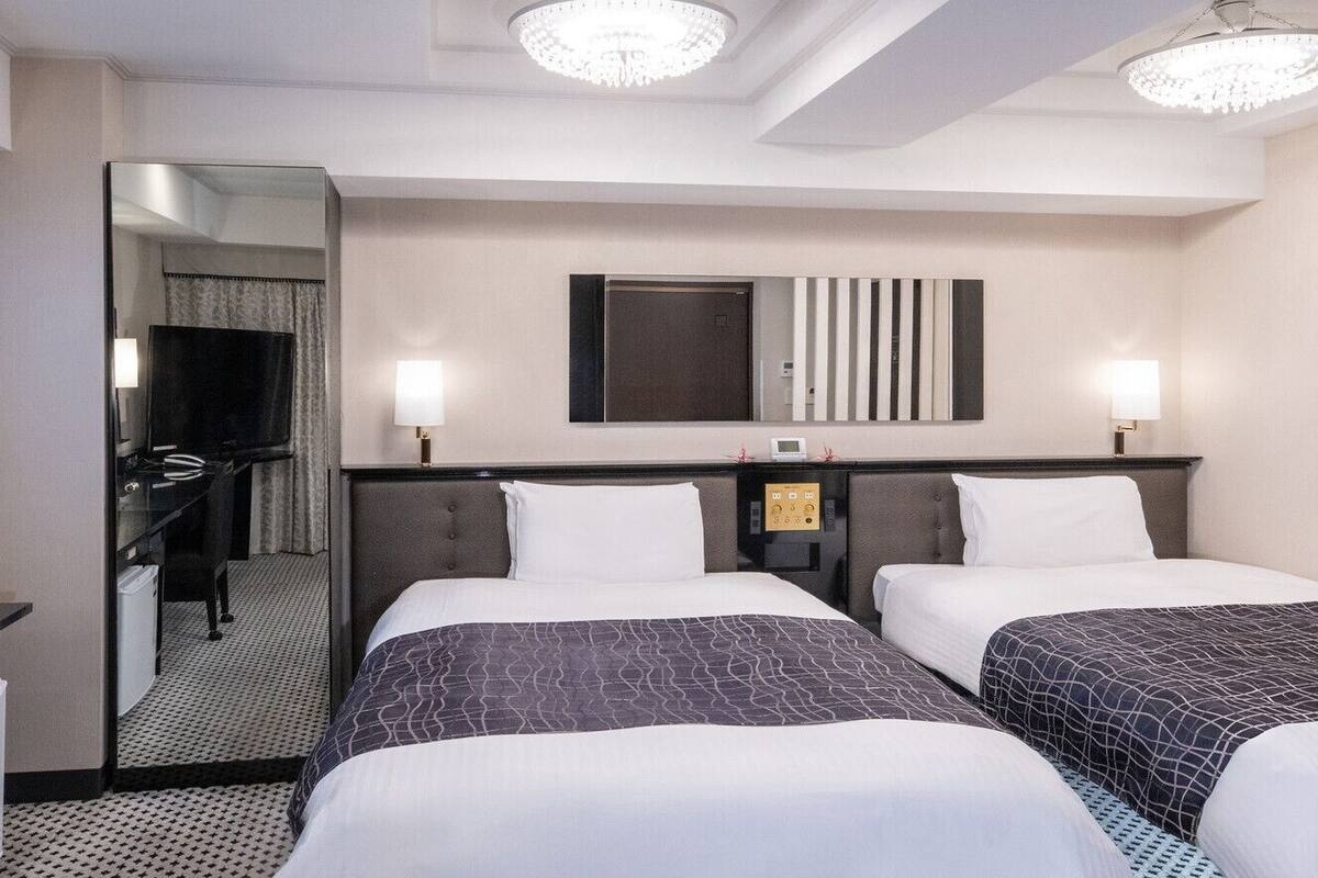 Une chambre d’hôtel avec deux lits, un miroir, une télévision et un bureau.