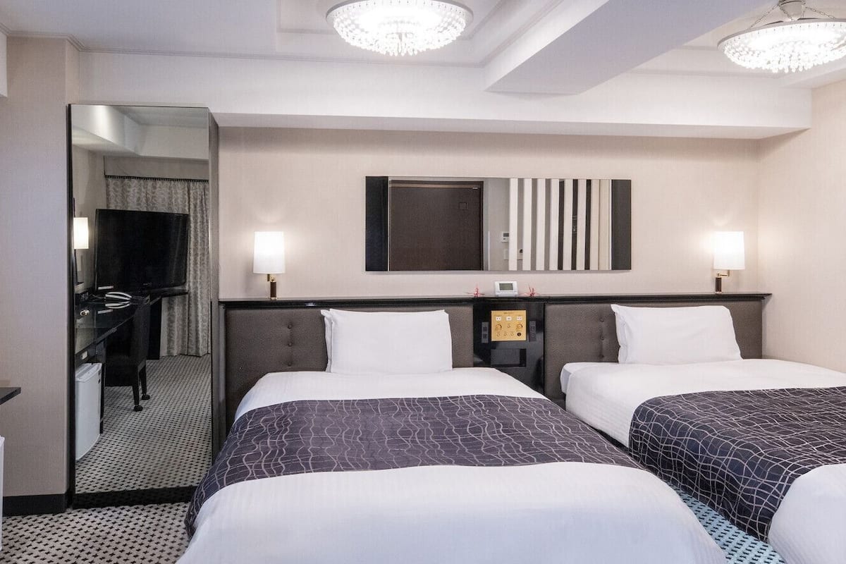 A hotel room with two beds, a mirror, a television, and a desk.