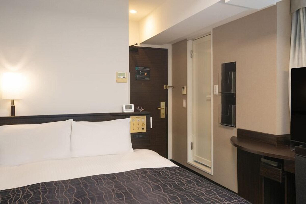 A hotel room with a bed, a television, a desk, and a shower.
