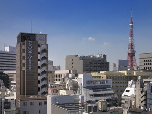 A hotel with multiple floors and balconies, surrounded by other buildings and a prominent tower in the background. - APA Hotel Shimbashi Onarimon (Tokyo)