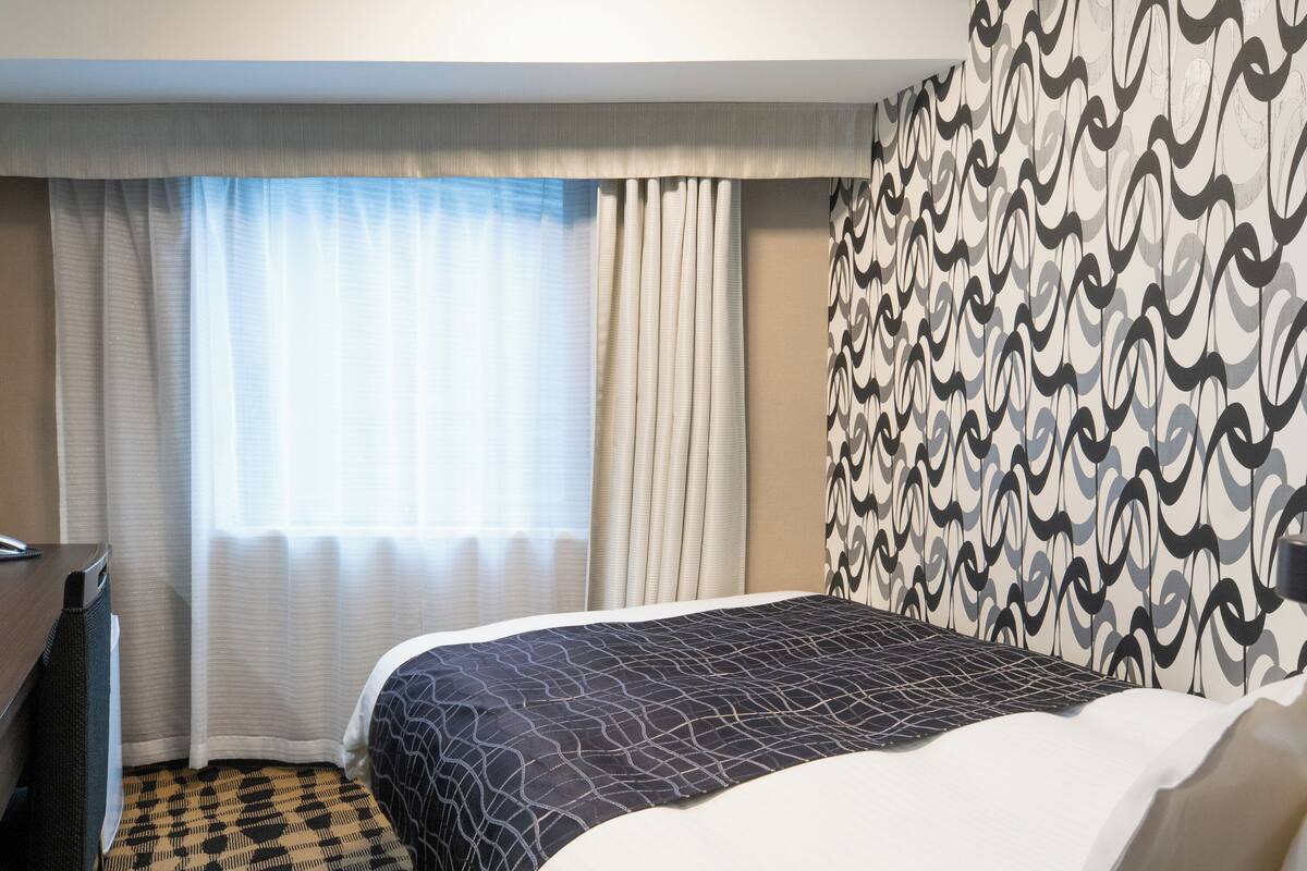 A hotel room with a bed, a desk, and a patterned wall.