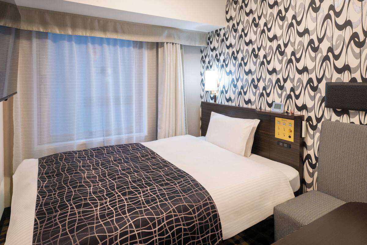 A hotel room with a large bed, a bedside table with a lamp, and a patterned wall.