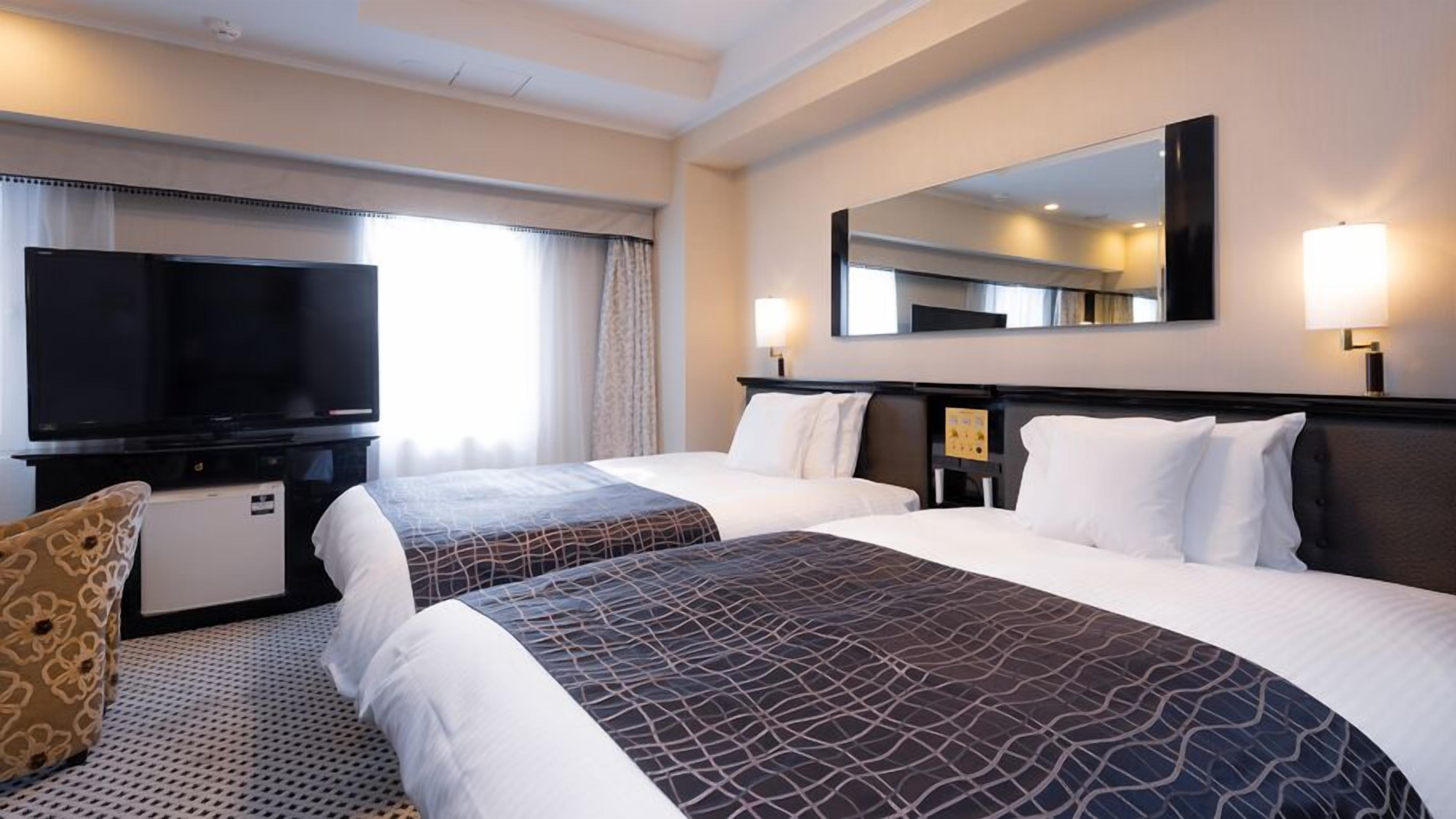 Een hotelkamer met twee bedden, een televisie, een bureau en een spiegel.