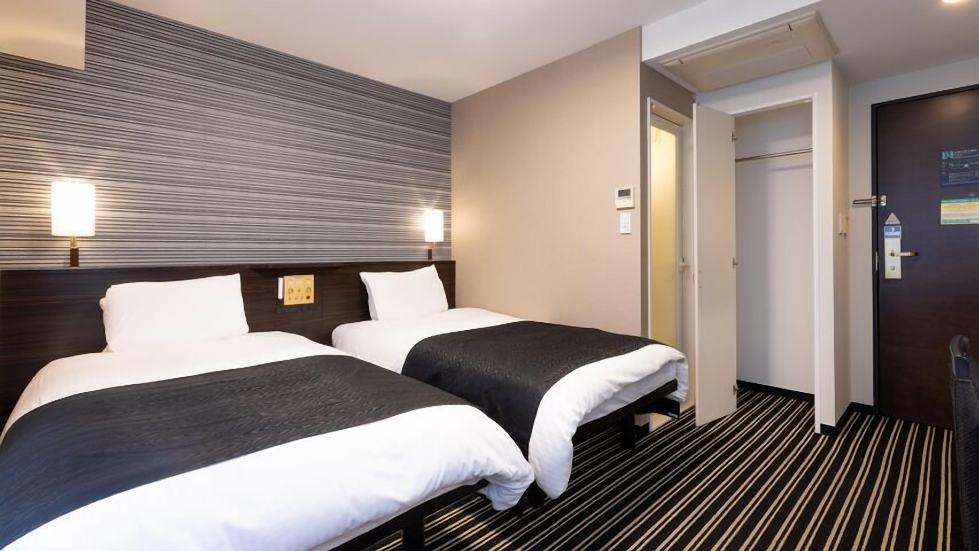 Een hotelkamer met twee bedden, een gestreept tapijt en een deur naar een andere kamer.