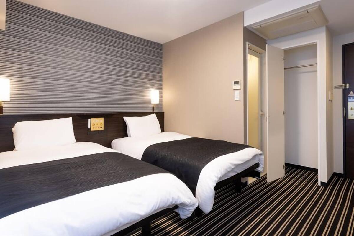Hotellihuone, jossa on kaksi sänkyä, raidallinen matto ja ovi, joka johtaa toiseen huoneeseen.
