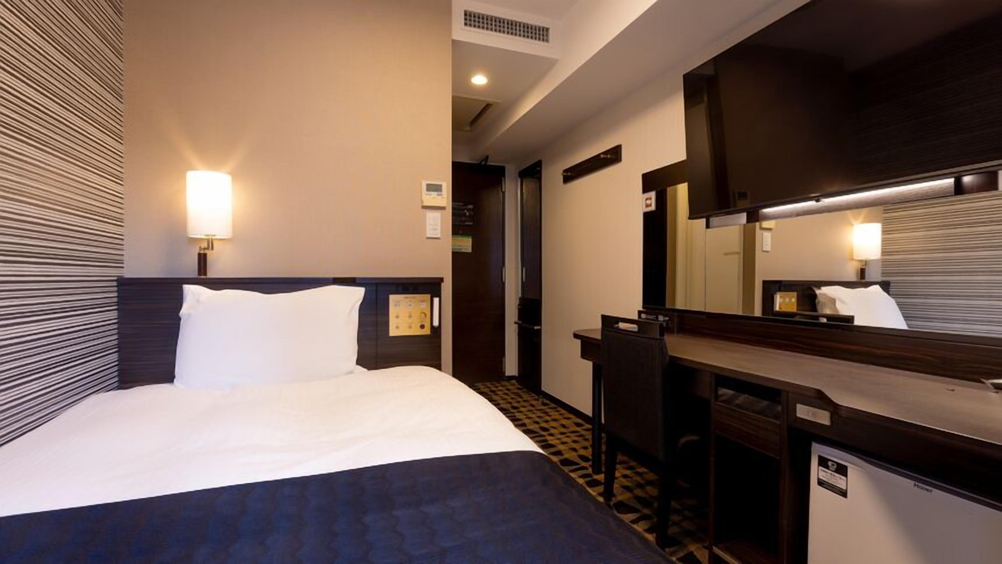 Een hotelkamer met een bed, bureau, stoel, spiegel en deur.
