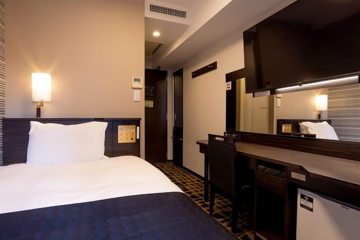 Une chambre d’hôtel avec un lit, un bureau, une chaise, un miroir et une porte.