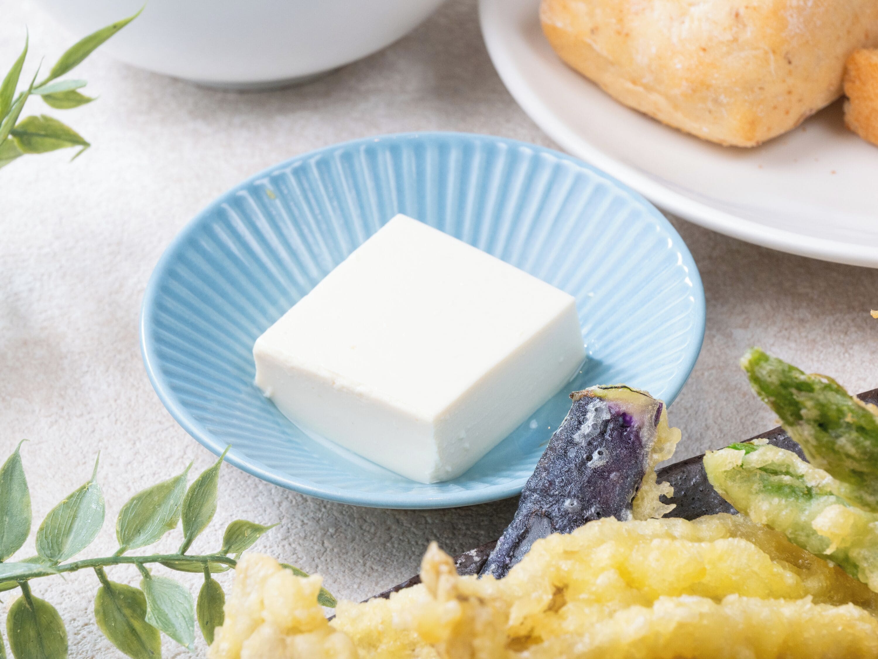 A blue plate with a white block of cheese, surrounded by various food items.