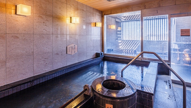 Un área de piscina interior moderna con pared de piedra, techo de madera y vistas al exterior a través de amplios ventanales.
