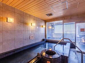 A modern indoor pool area with a stone wall, a wooden ceiling, and a view of the outside through large windows.