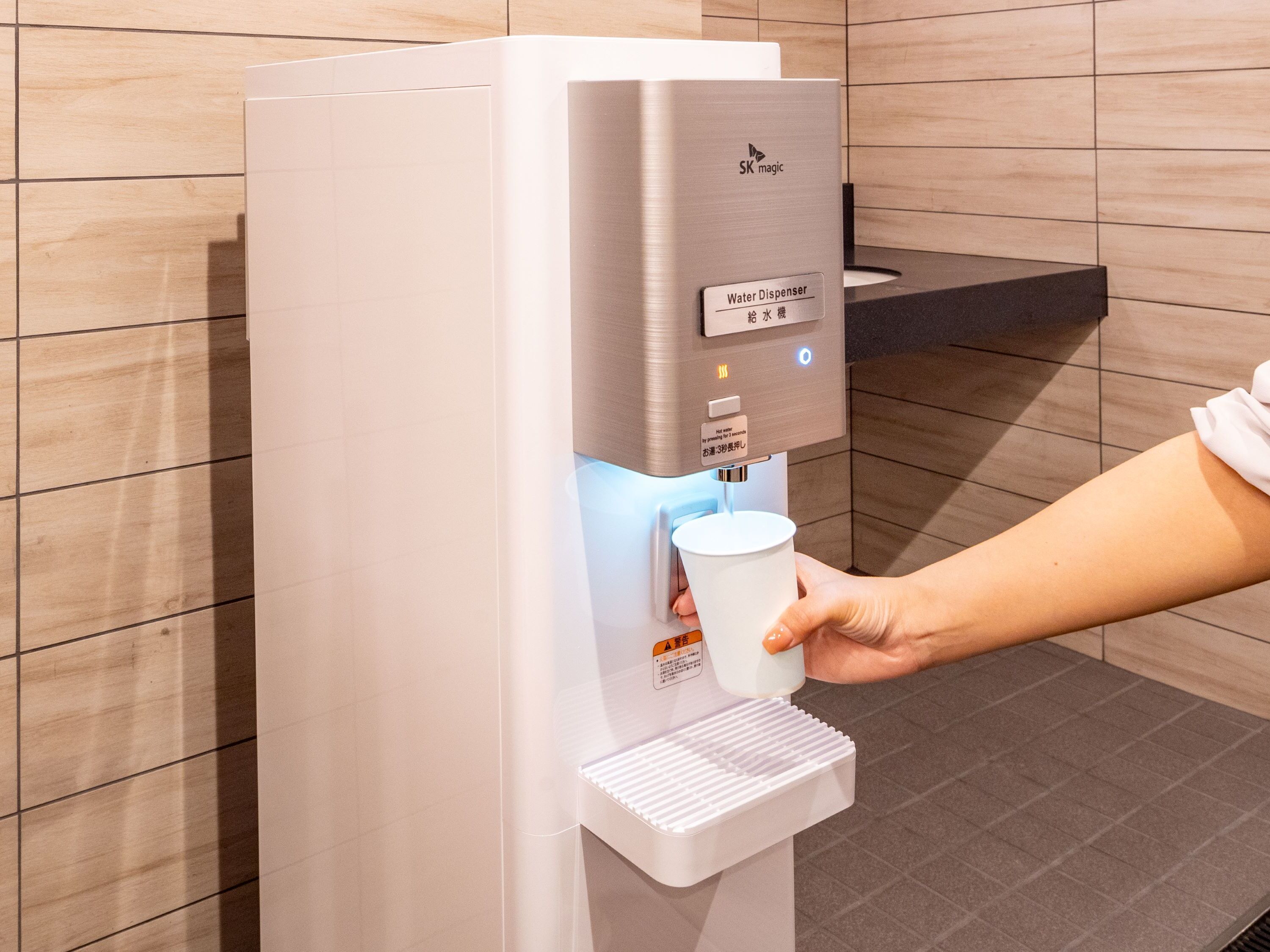 A water dispenser with a cup holder, a digital display, and a warning label.