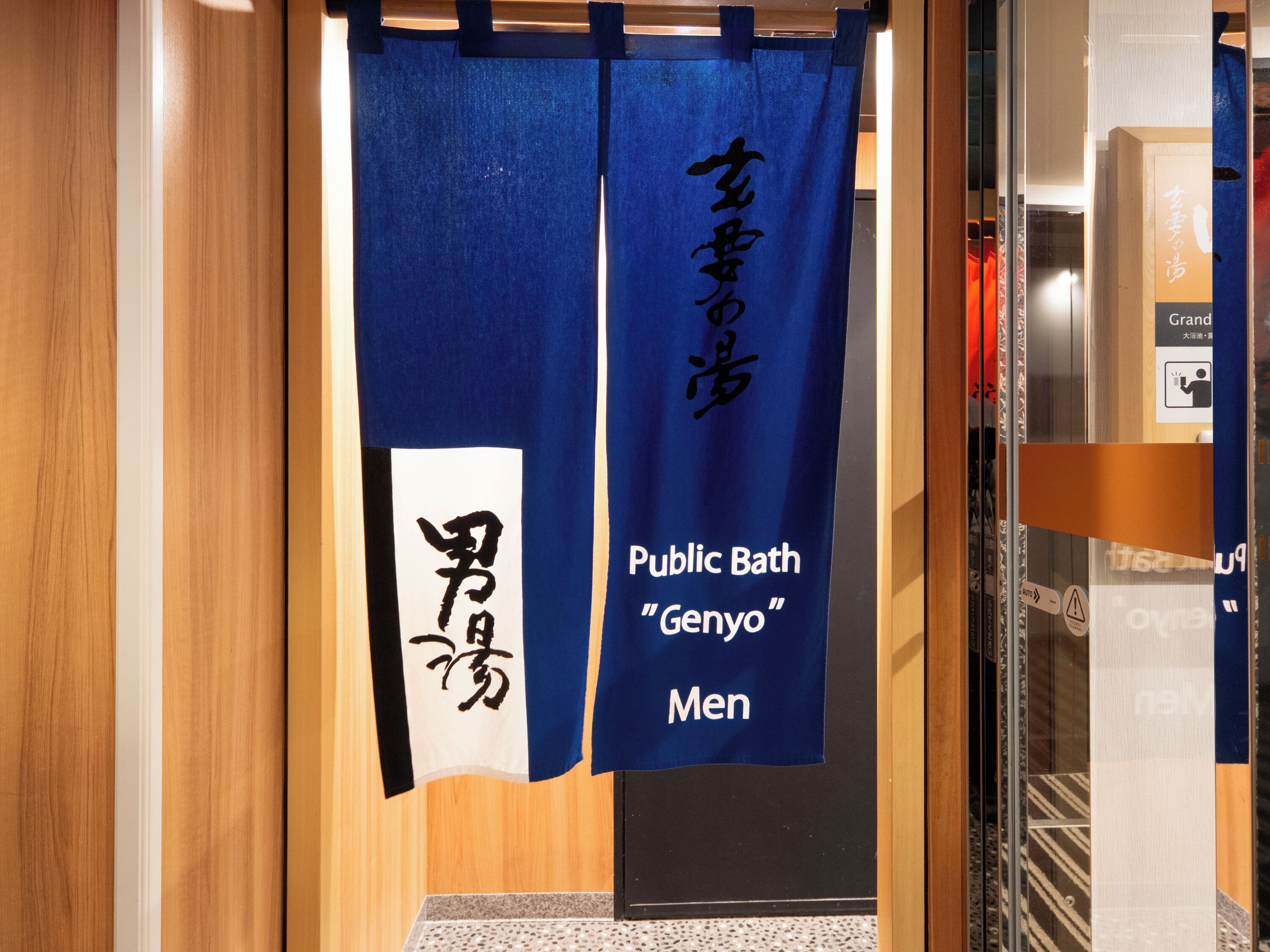 A public bath entrance with a blue curtain displaying Japanese characters and the words "Public Bath 'Genyo' Men".