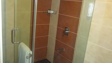 Cabina de ducha con paredes de vidrio, un cabezal de ducha de mano, un perchero y una puerta de vidrio.