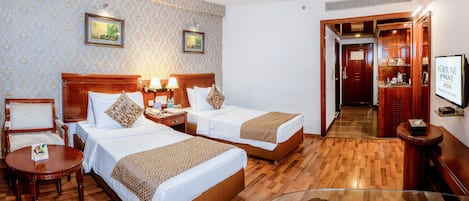 A hotel room with two beds, a wooden floor, a desk, and a TV.