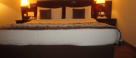 A neatly made bed with a dark headboard and white bedding, flanked by two bedside tables with lamps, in a room with a warm ambiance.