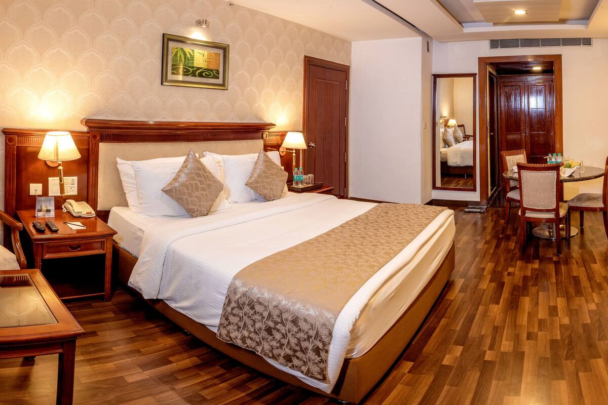 Une chambre d’hôtel avec un grand lit, deux tables de chevet, un bureau avec une chaise, un miroir et une armoire.
