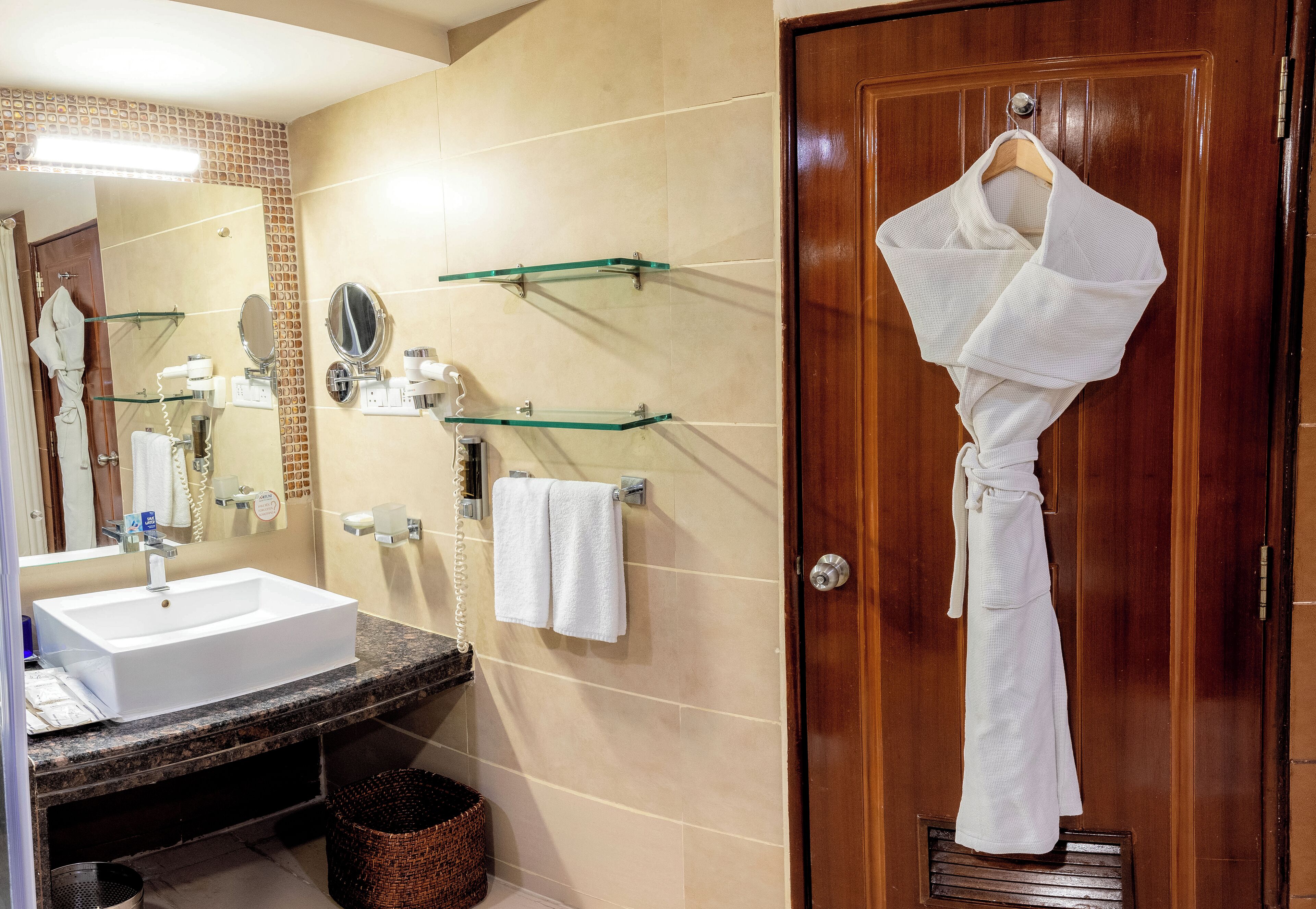 A bathroom with a sink, mirror, towel rack, and a robe hanging on a door.