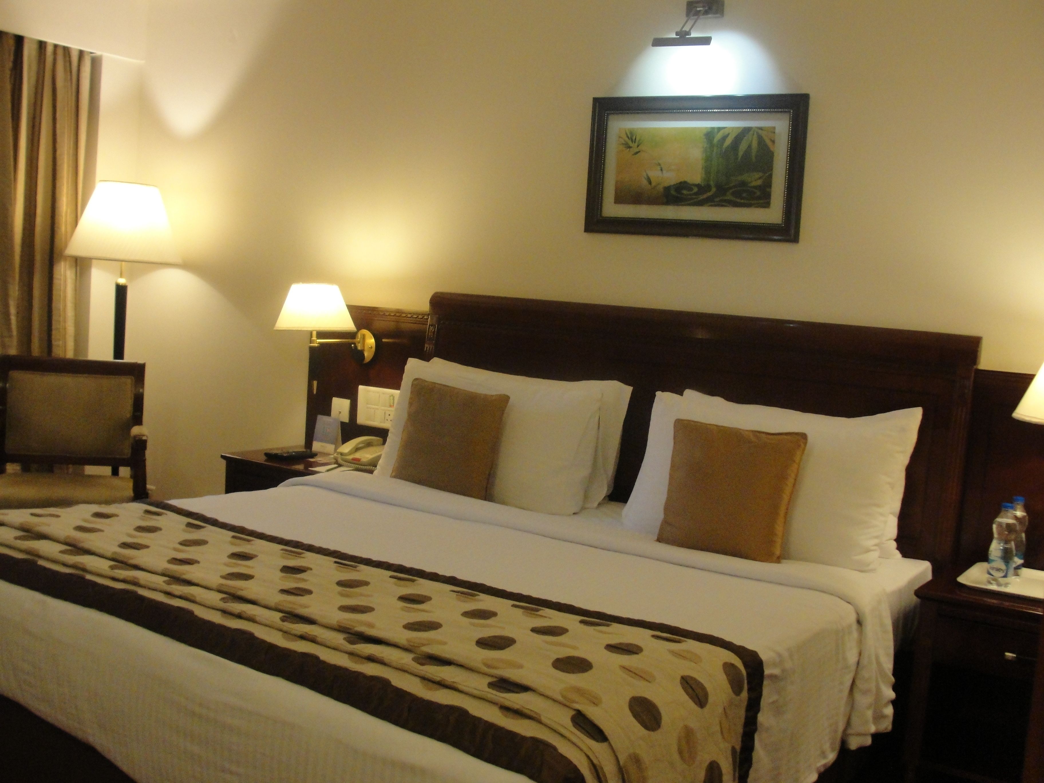 A hotel room with a large bed, two bedside tables, a nightstand, a chair, and a painting on the wall.