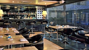 A modern bar area with high stools, a bar counter with bottles, and a large window with blinds. - Fortune JP Palace, Mysore - Member ITC Hotels' Group (Mysore)