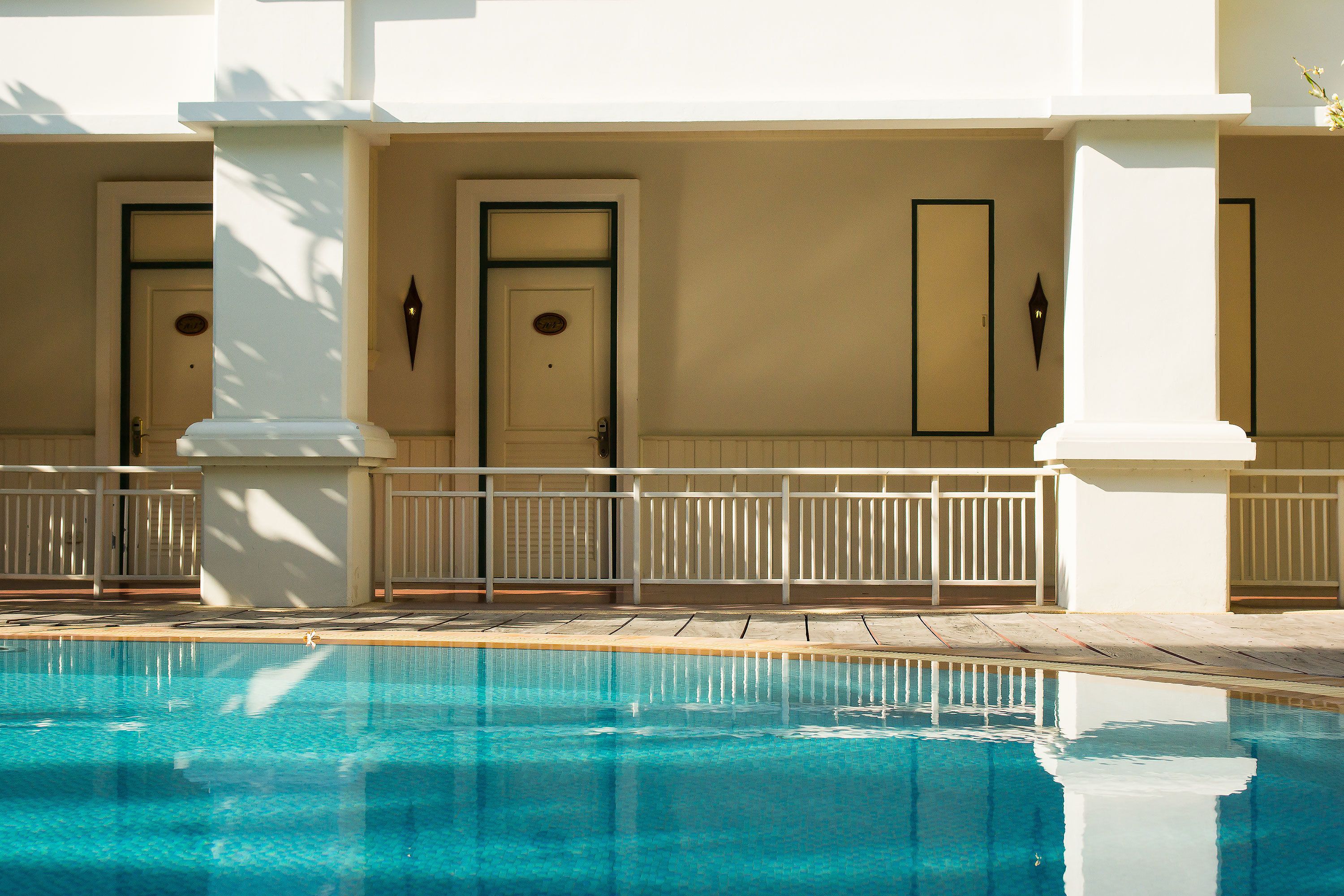 A swimming pool with a white fence and doors in the background.