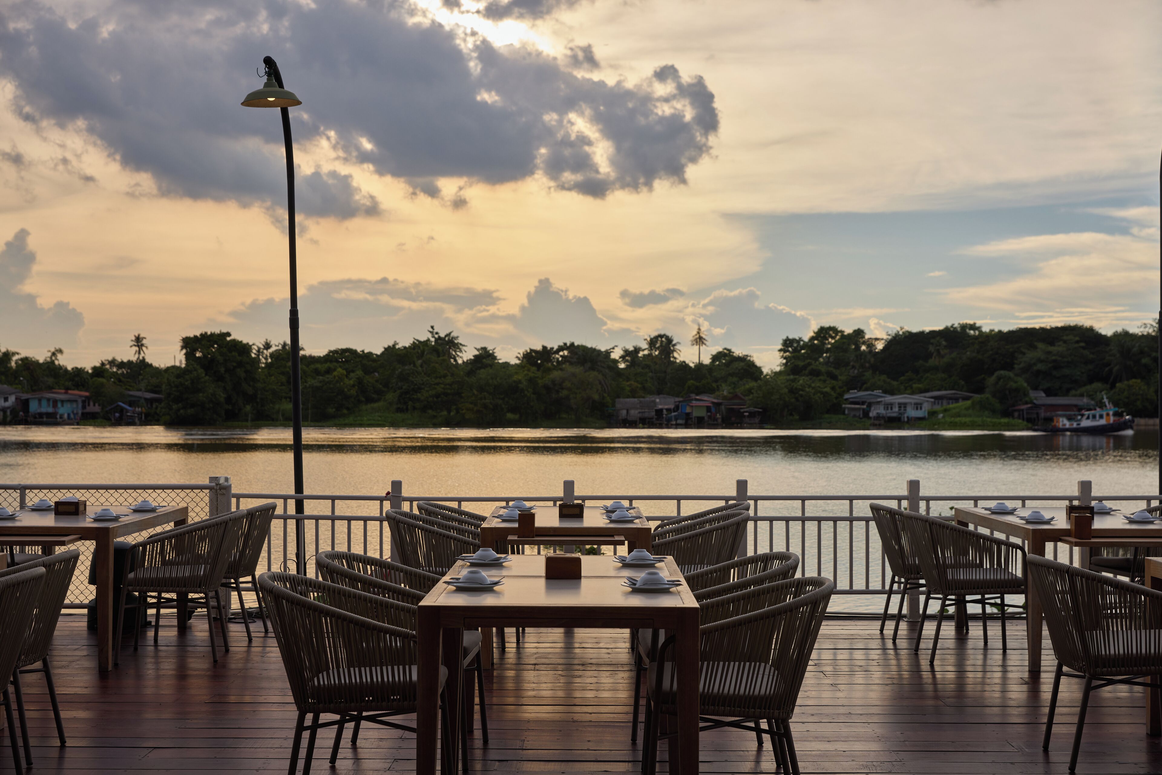 A restaurant deck with tables and chairs facing a lake, surrounded by a fence, and a lamp post is visible.