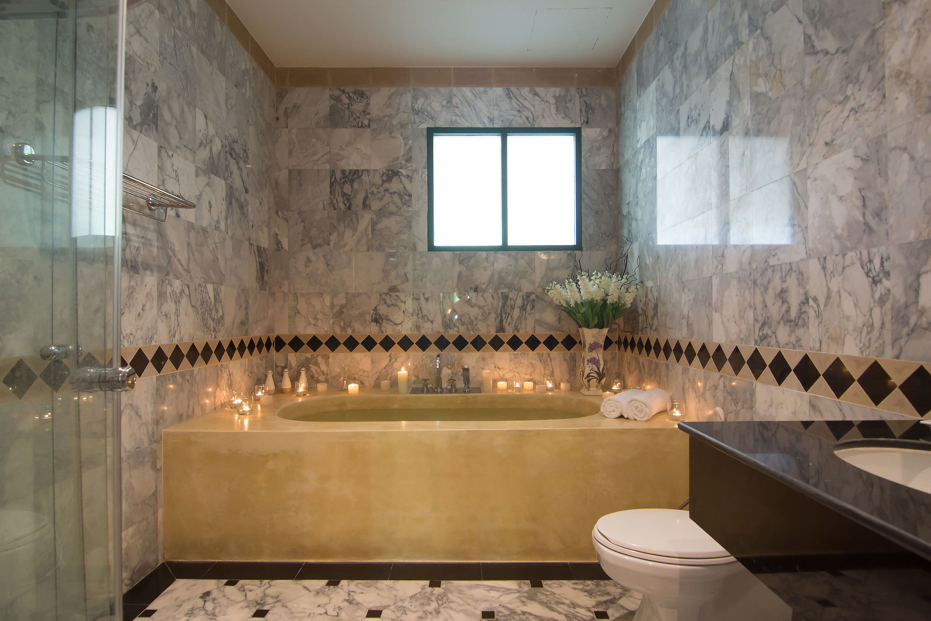 A bathroom with a marble wall, a bathtub, a toilet, and a sink.