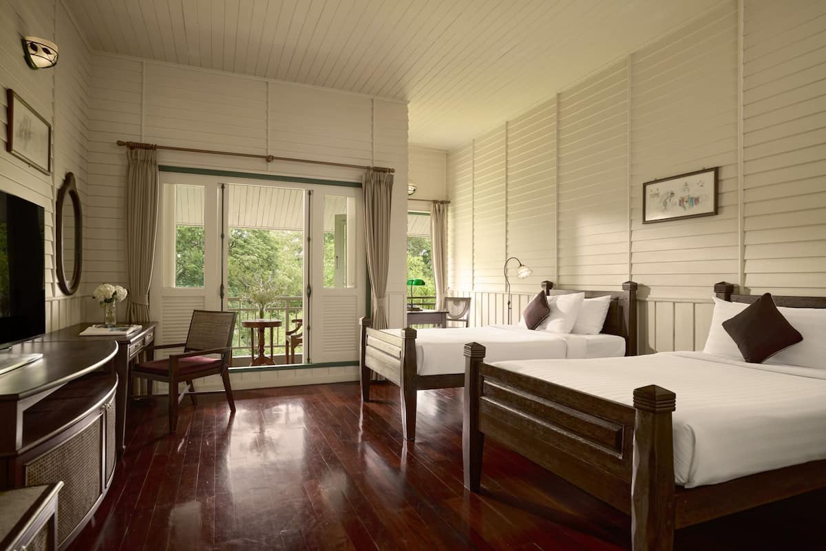 Habitación de hotel con dos camas de madera, un escritorio con silla, televisión y una ventana con cortinas.